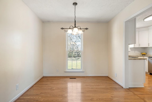 unfurnished dining area with an inviting chandelier, light hardwood / wood-style floors, a textured ceiling, and a wealth of natural light