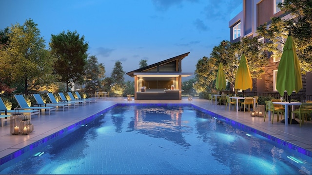 pool at dusk featuring exterior fireplace and a patio