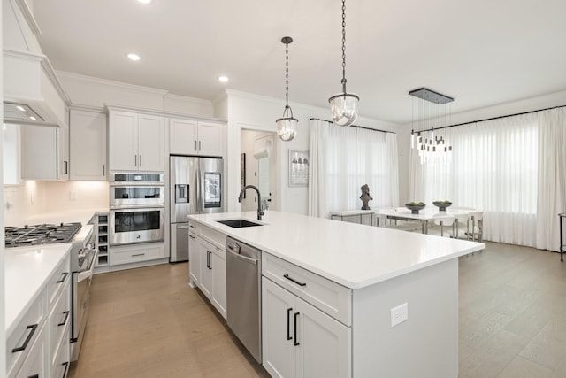 kitchen with sink, white cabinetry, hanging light fixtures, stainless steel appliances, and an island with sink