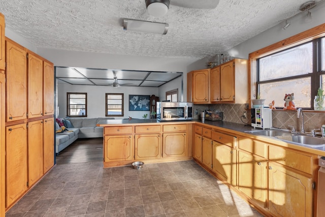 kitchen featuring sink, a textured ceiling, appliances with stainless steel finishes, kitchen peninsula, and backsplash