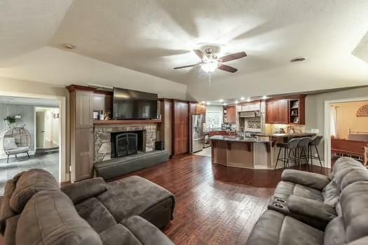 living room featuring a stone fireplace, dark hardwood / wood-style floors, and ceiling fan