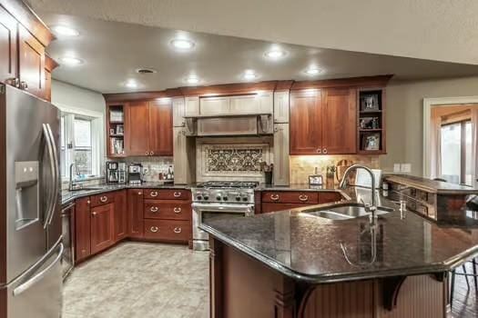 kitchen with sink, dark stone countertops, kitchen peninsula, stainless steel appliances, and plenty of natural light