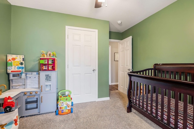 bedroom with a nursery area, light colored carpet, and ceiling fan