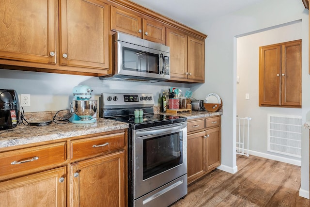 kitchen with light stone counters, appliances with stainless steel finishes, and dark hardwood / wood-style flooring