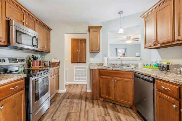 kitchen featuring pendant lighting, sink, hardwood / wood-style flooring, stainless steel appliances, and light stone counters