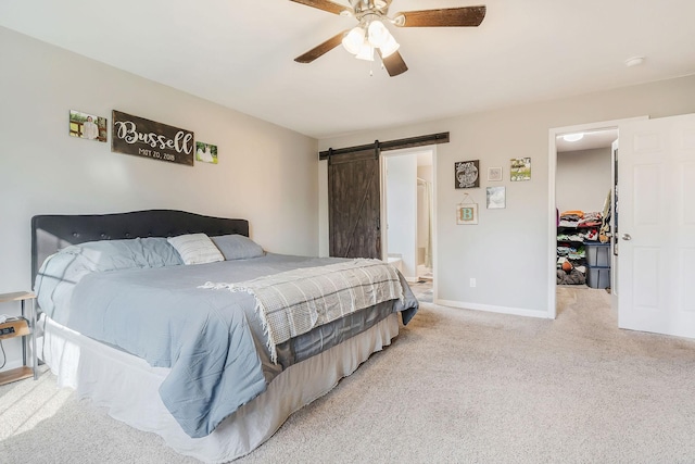 bedroom with ceiling fan, a barn door, light carpet, a walk in closet, and a closet