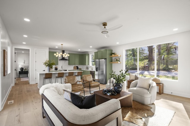 living room with ceiling fan with notable chandelier, sink, and light wood-type flooring