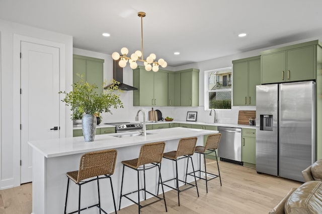 kitchen with light hardwood / wood-style flooring, green cabinets, a kitchen island with sink, stainless steel appliances, and wall chimney exhaust hood