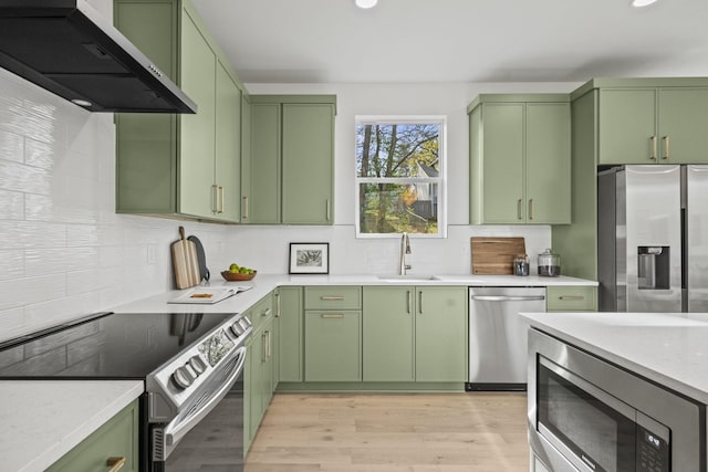 kitchen with green cabinetry, appliances with stainless steel finishes, sink, and wall chimney range hood