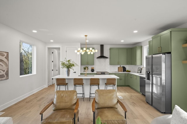 kitchen featuring decorative backsplash, hanging light fixtures, green cabinetry, stainless steel appliances, and wall chimney range hood