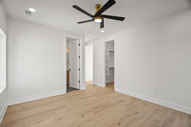 unfurnished bedroom featuring a spacious closet, a closet, ceiling fan, and light wood-type flooring