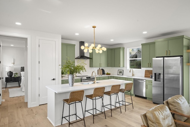 kitchen featuring wall chimney range hood, decorative light fixtures, green cabinetry, and appliances with stainless steel finishes