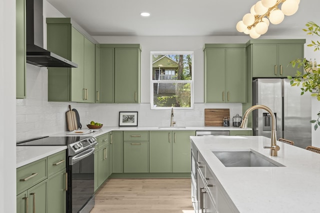 kitchen with stainless steel appliances, sink, green cabinetry, and wall chimney exhaust hood