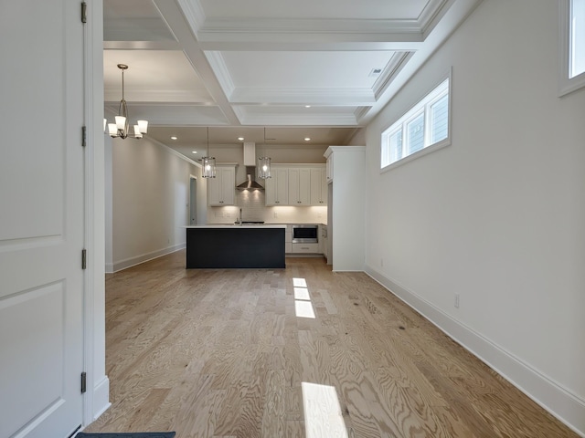 unfurnished living room with coffered ceiling, an inviting chandelier, crown molding, light wood-type flooring, and beam ceiling