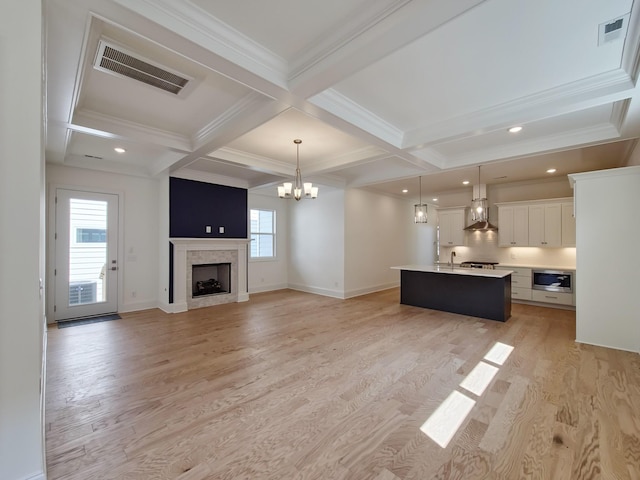 unfurnished living room featuring an inviting chandelier, coffered ceiling, ornamental molding, light hardwood / wood-style floors, and beamed ceiling