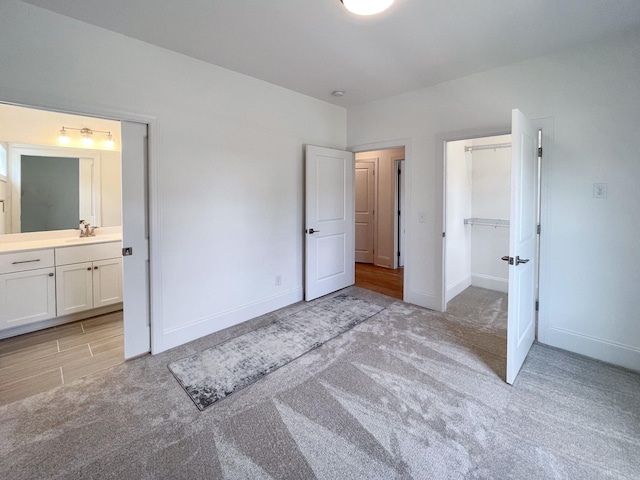 unfurnished bedroom with sink, a spacious closet, light carpet, ensuite bath, and a closet