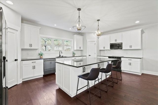 kitchen featuring sink, stainless steel appliances, white cabinets, a kitchen island, and decorative light fixtures