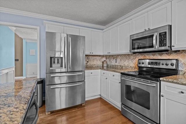 kitchen featuring stainless steel appliances, white cabinetry, light stone counters, and crown molding