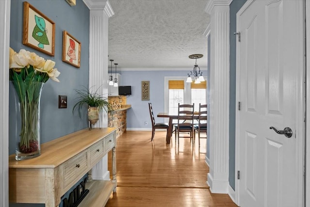 hall featuring ornate columns, crown molding, a textured ceiling, and light wood-type flooring