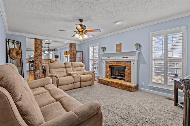 carpeted living room with ornamental molding, a stone fireplace, decorative columns, and a textured ceiling