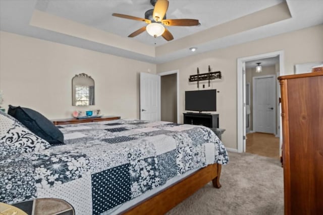 bedroom with a raised ceiling, light colored carpet, and ceiling fan