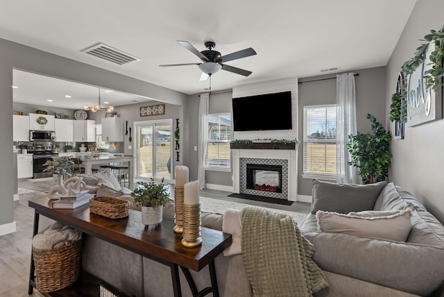 living room with a tiled fireplace, light hardwood / wood-style floors, and ceiling fan