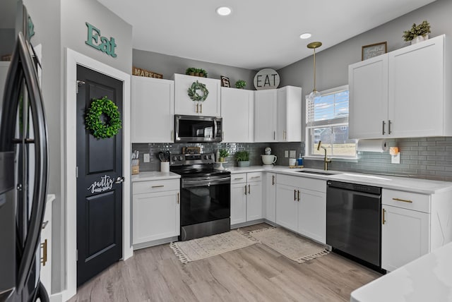 kitchen with appliances with stainless steel finishes, white cabinetry, sink, hanging light fixtures, and light wood-type flooring