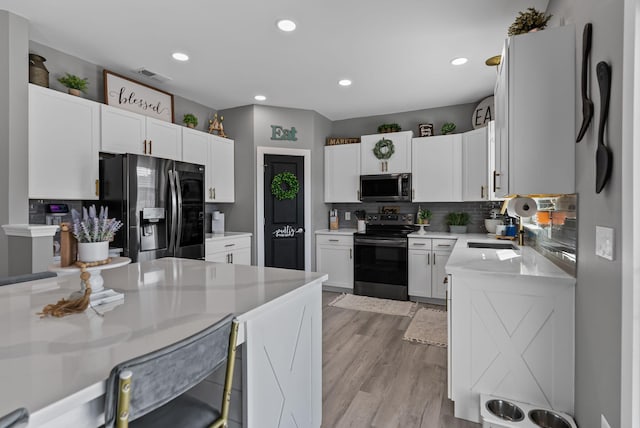 kitchen featuring white cabinetry, light stone counters, light hardwood / wood-style flooring, appliances with stainless steel finishes, and decorative backsplash