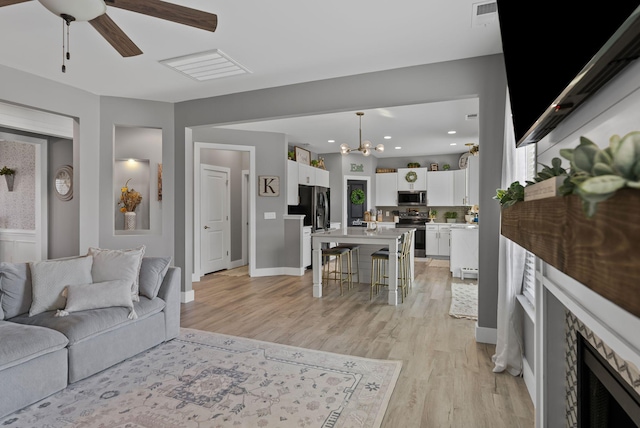 living room featuring a stone fireplace, ceiling fan with notable chandelier, and light wood-type flooring