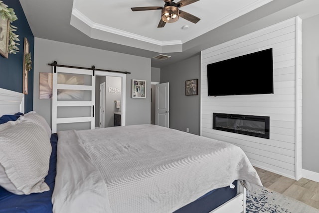 bedroom featuring a tray ceiling, light hardwood / wood-style floors, a barn door, and ceiling fan