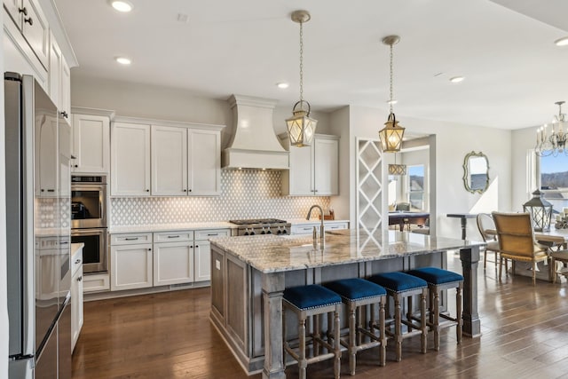 kitchen with premium range hood, white cabinetry, appliances with stainless steel finishes, and a center island with sink