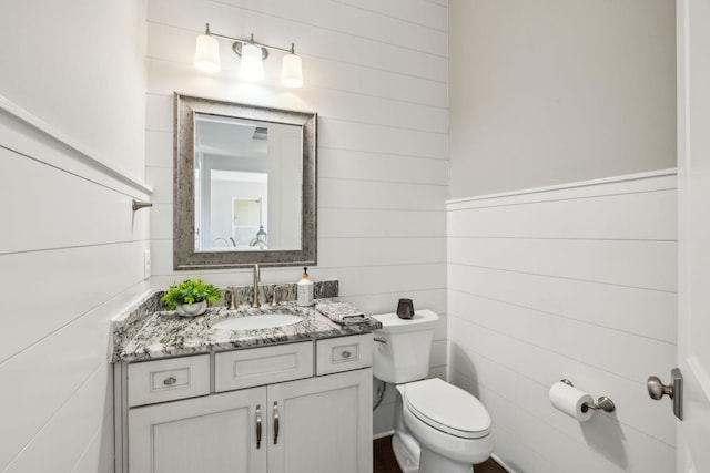 bathroom featuring vanity, toilet, and wood walls