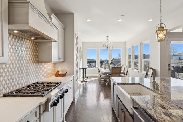 kitchen with white cabinetry, stainless steel appliances, tasteful backsplash, custom range hood, and decorative light fixtures