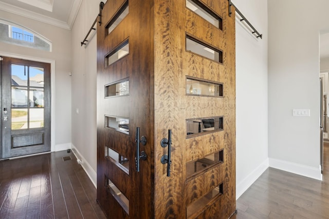 entryway with dark wood-type flooring, ornamental molding, and a barn door