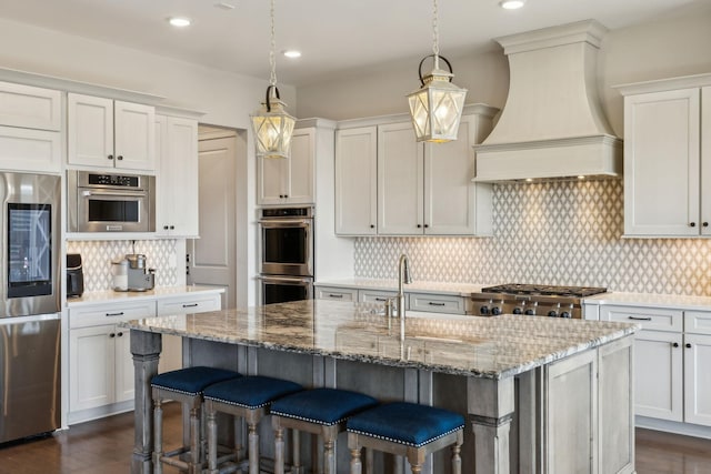 kitchen with stainless steel appliances, premium range hood, a kitchen island with sink, and white cabinetry