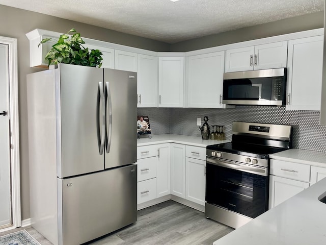 kitchen with white cabinetry, appliances with stainless steel finishes, backsplash, and light wood-type flooring