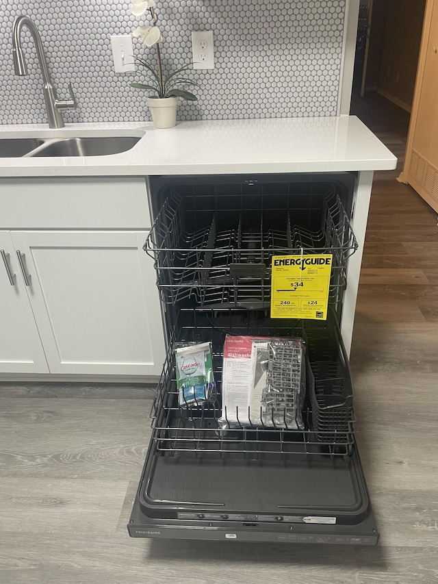 details featuring dishwashing machine, sink, dark wood-type flooring, white cabinetry, and decorative backsplash