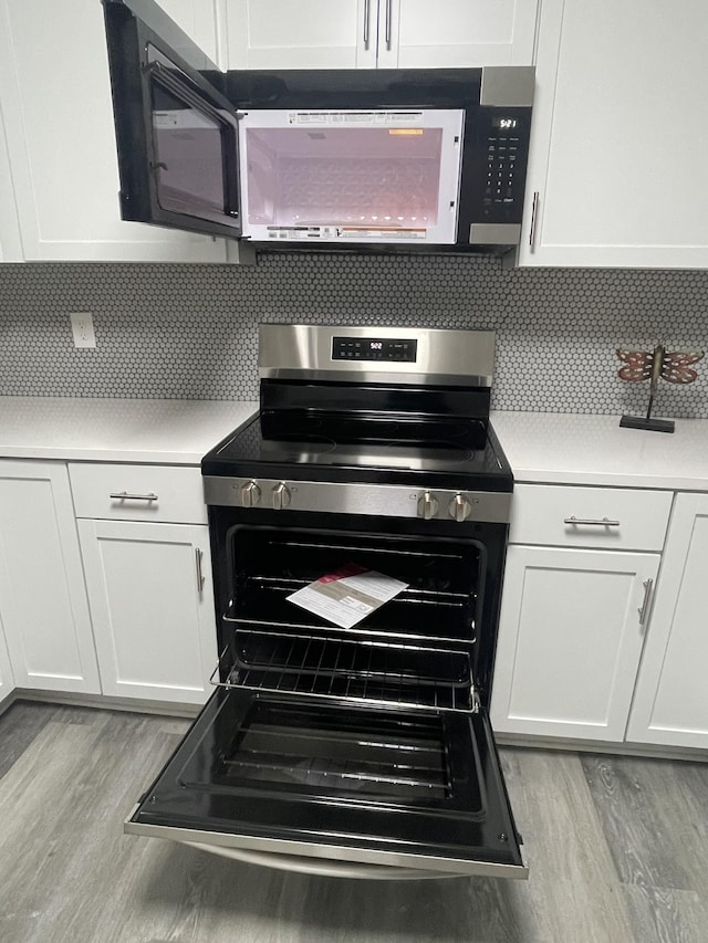 kitchen with tasteful backsplash, stainless steel range with electric stovetop, light wood-type flooring, and white cabinets