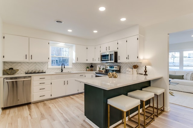 kitchen featuring sink, a breakfast bar area, stainless steel appliances, white cabinets, and kitchen peninsula