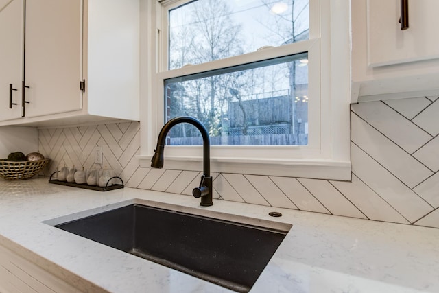 interior details with white cabinetry, light stone countertops, sink, and backsplash