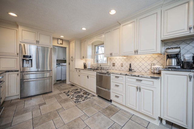 kitchen featuring sink, washer and clothes dryer, stainless steel appliances, white cabinets, and dark stone counters