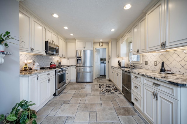 kitchen with white cabinetry, stainless steel appliances, light stone countertops, and backsplash