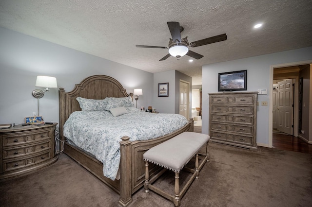 bedroom with ceiling fan, connected bathroom, dark carpet, and a textured ceiling