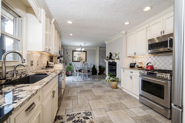 kitchen featuring sink, crown molding, appliances with stainless steel finishes, hanging light fixtures, and light stone counters