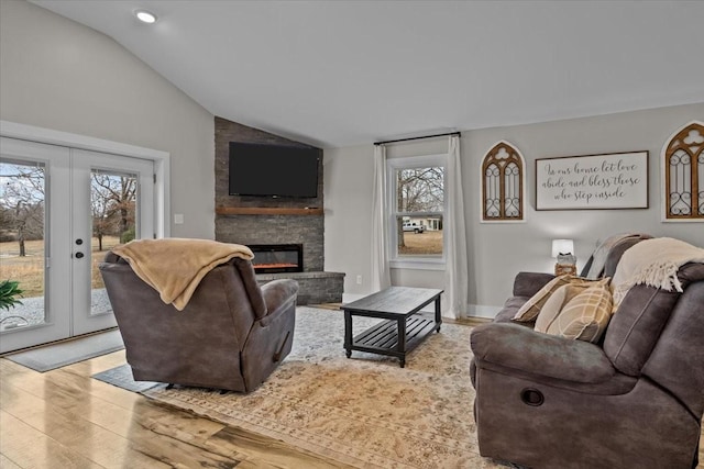 living room featuring lofted ceiling, light hardwood / wood-style flooring, a large fireplace, and french doors