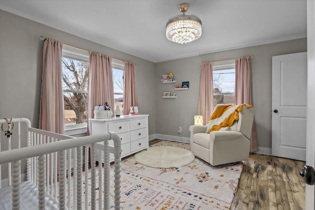 bedroom featuring a crib, hardwood / wood-style floors, and an inviting chandelier