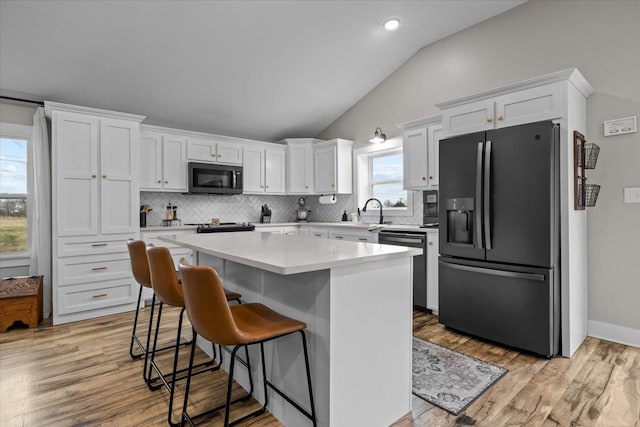 kitchen with white cabinetry, dishwashing machine, a center island, and black refrigerator with ice dispenser