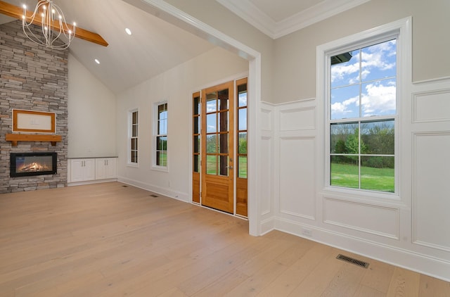 doorway to outside featuring crown molding, high vaulted ceiling, a notable chandelier, a fireplace, and light hardwood / wood-style floors