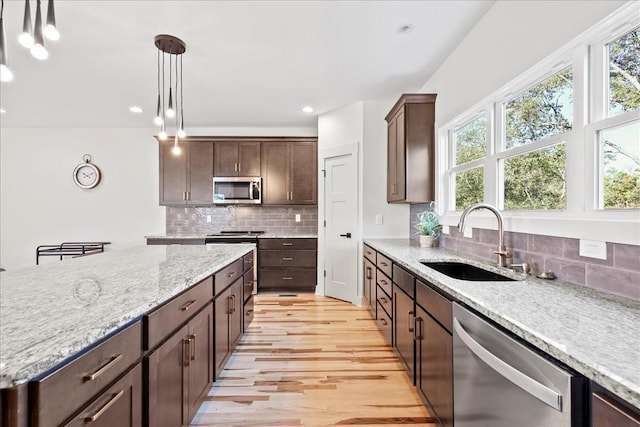 kitchen with sink, hanging light fixtures, dark brown cabinets, stainless steel appliances, and light stone countertops