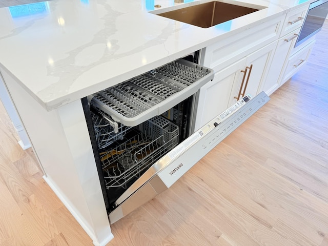 interior details with light stone counters, white cabinetry, light hardwood / wood-style floors, and sink